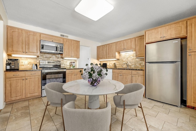 kitchen with stainless steel appliances, light brown cabinetry, sink, and backsplash