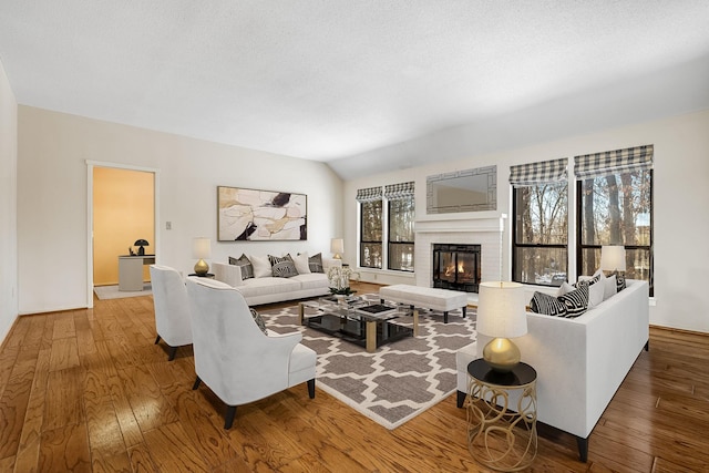 living room featuring hardwood / wood-style flooring, vaulted ceiling, a textured ceiling, and a fireplace