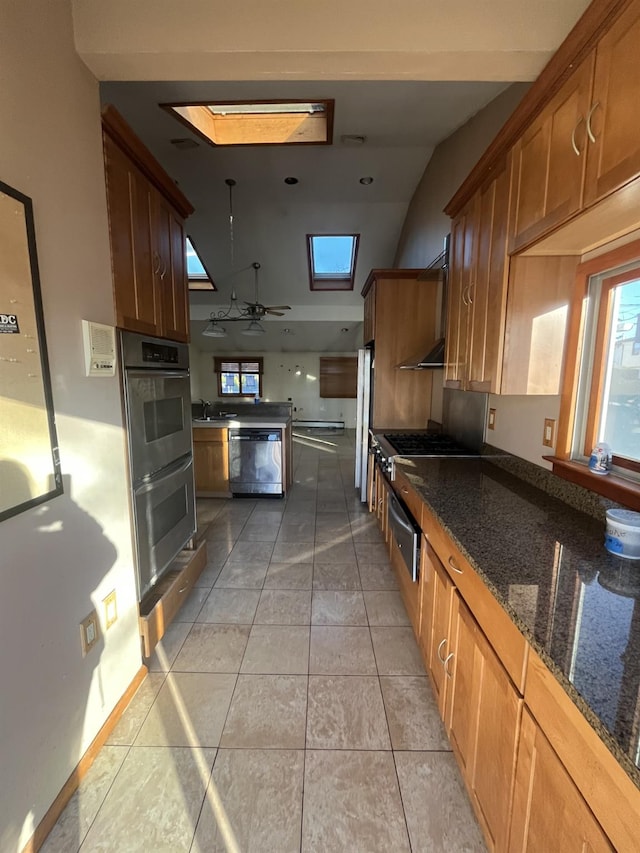 kitchen featuring appliances with stainless steel finishes, a skylight, sink, dark stone countertops, and light tile patterned floors