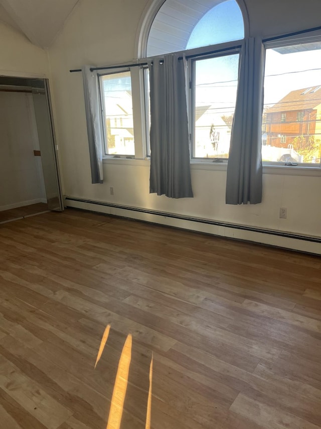 unfurnished bedroom featuring lofted ceiling, hardwood / wood-style floors, and baseboard heating