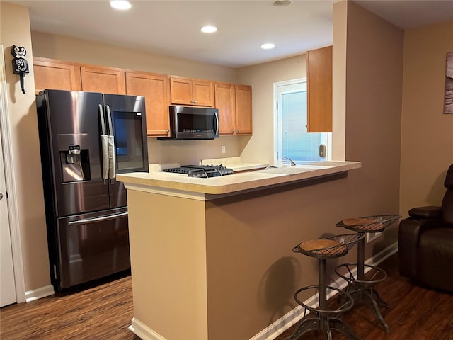 kitchen featuring hardwood / wood-style floors, a kitchen breakfast bar, kitchen peninsula, stainless steel appliances, and light brown cabinets