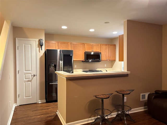 kitchen featuring appliances with stainless steel finishes, a breakfast bar, dark hardwood / wood-style flooring, and kitchen peninsula