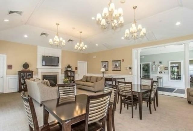 carpeted dining space with vaulted ceiling, an inviting chandelier, and a fireplace