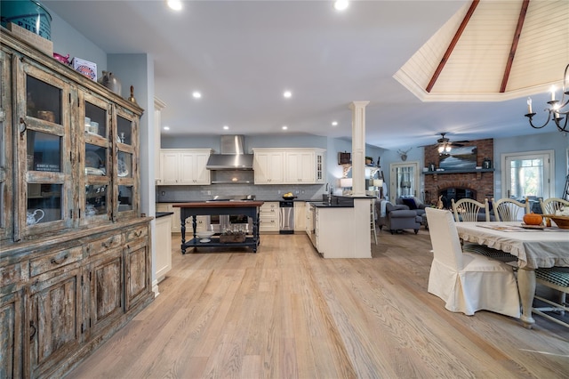 kitchen with wall chimney exhaust hood, tasteful backsplash, vaulted ceiling, light wood-type flooring, and a fireplace