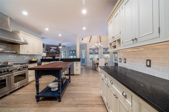 kitchen featuring hanging light fixtures, decorative columns, range with two ovens, wall chimney exhaust hood, and light wood-type flooring