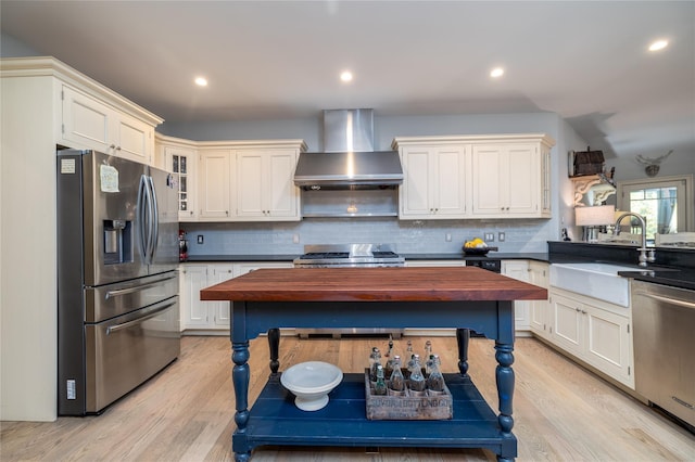 kitchen featuring sink, light wood-type flooring, wall chimney exhaust hood, and appliances with stainless steel finishes