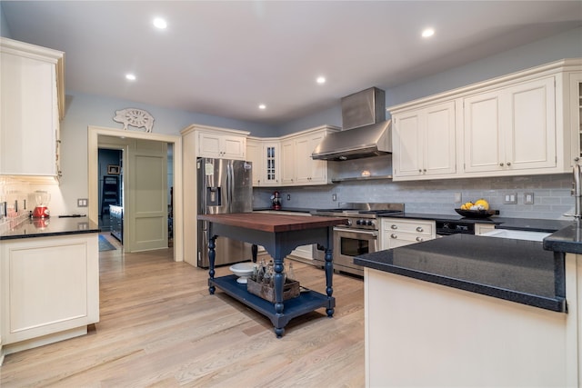 kitchen with light wood-type flooring, appliances with stainless steel finishes, kitchen peninsula, decorative backsplash, and wall chimney range hood