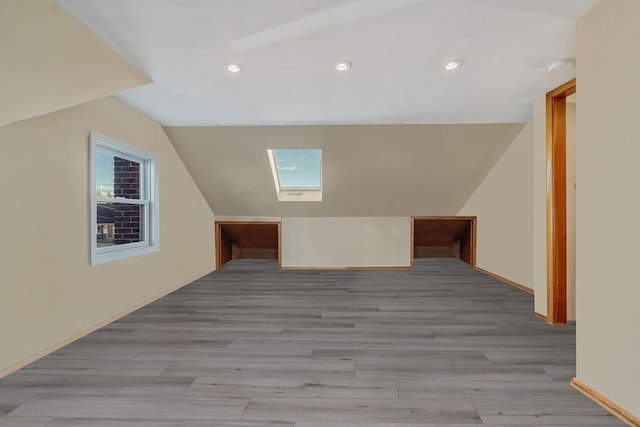 additional living space with vaulted ceiling with skylight and light hardwood / wood-style floors