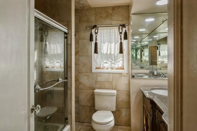 full bathroom with combined bath / shower with glass door, tile walls, tile patterned flooring, vanity, and toilet