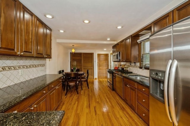 kitchen featuring sink, light hardwood / wood-style flooring, dark stone counters, and appliances with stainless steel finishes