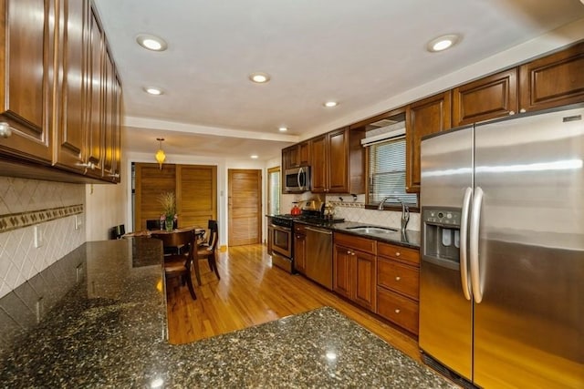 kitchen with appliances with stainless steel finishes, sink, dark stone counters, and decorative backsplash