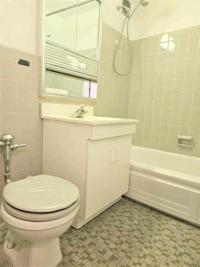 full bathroom featuring vanity, tiled shower / bath, tile walls, and toilet