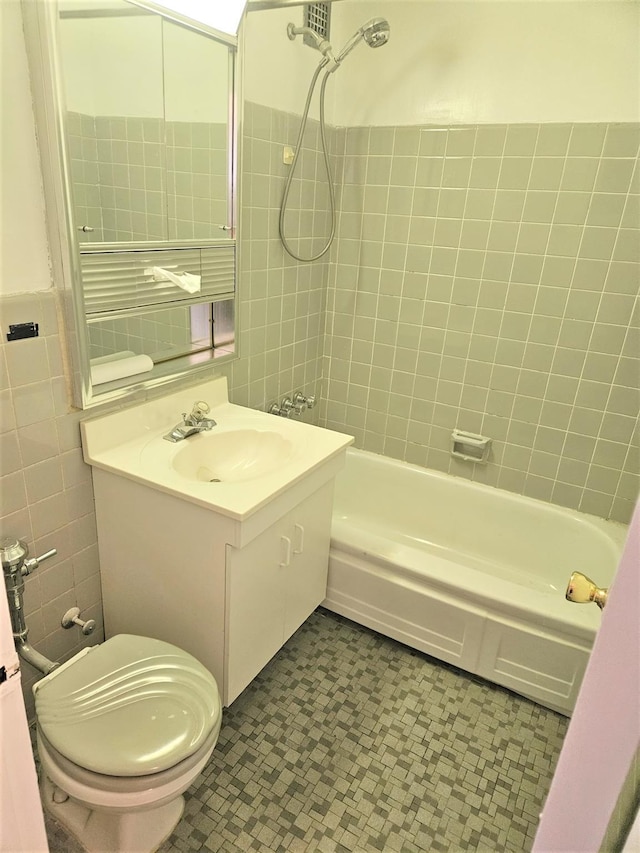 full bathroom featuring tile walls, tiled shower / bath, vanity, and toilet