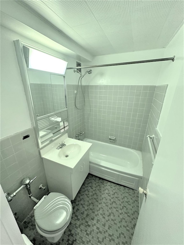 full bathroom with tile walls, vanity, tiled shower / bath combo, and toilet