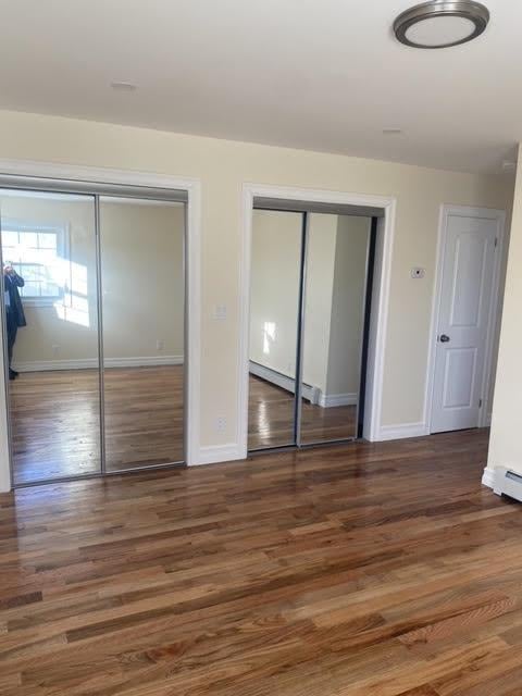 unfurnished bedroom featuring multiple closets, dark hardwood / wood-style floors, and baseboard heating