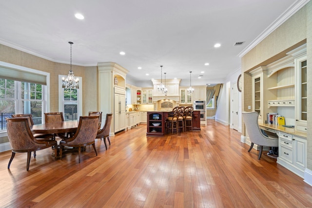 dining room with a notable chandelier, ornamental molding, built in desk, and light wood-type flooring