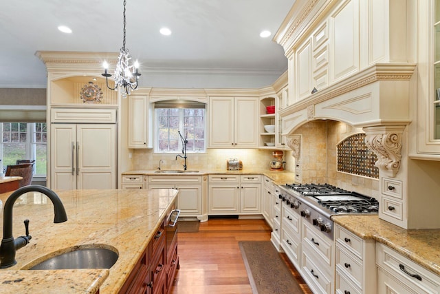 kitchen with light stone counters, hanging light fixtures, sink, and stainless steel gas cooktop