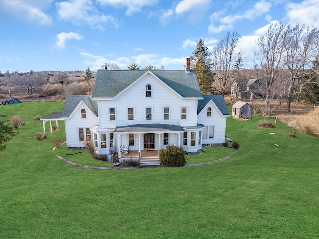 back of property featuring covered porch, a yard, a chimney, and a storage unit