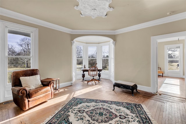 living area featuring baseboards, light wood-style flooring, visible vents, and crown molding