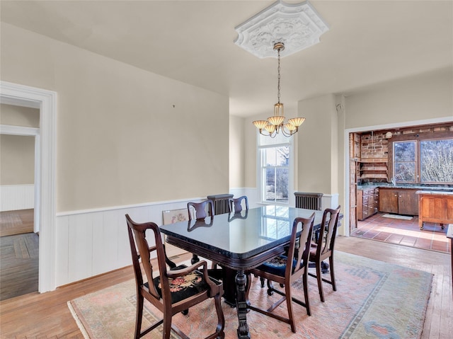 dining room featuring light wood-type flooring, wainscoting, and an inviting chandelier