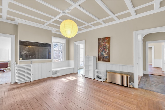 unfurnished living room featuring a wainscoted wall, coffered ceiling, radiator heating unit, and wood finished floors