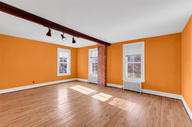 unfurnished room with baseboards, track lighting, light wood-style flooring, and radiator