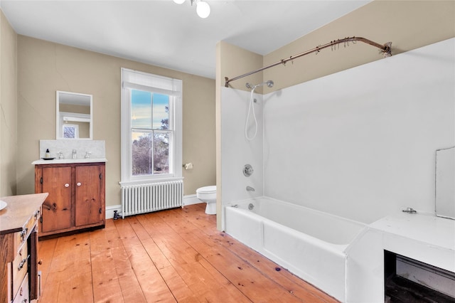 full bath with toilet, radiator heating unit, wood finished floors,  shower combination, and vanity