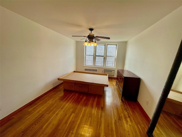 unfurnished bedroom featuring hardwood / wood-style floors, a wall unit AC, radiator, and ceiling fan