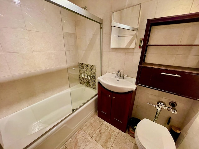 full bathroom featuring combined bath / shower with glass door, tile walls, decorative backsplash, vanity, and toilet