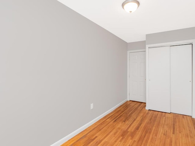 unfurnished bedroom featuring light wood finished floors, baseboards, and a closet