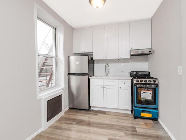 kitchen with stove, a sink, white cabinets, light countertops, and freestanding refrigerator