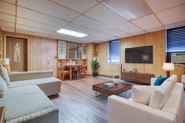 living room with hardwood / wood-style flooring, a paneled ceiling, and wood walls