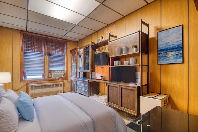 bedroom featuring a drop ceiling, radiator heating unit, and wood walls