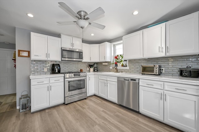 kitchen with stainless steel appliances, sink, light hardwood / wood-style flooring, and white cabinets