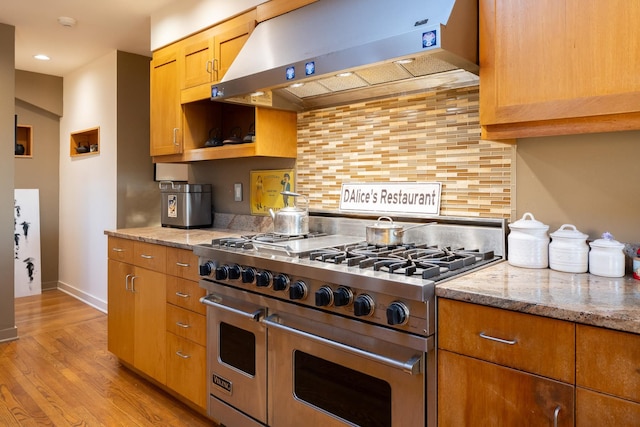 kitchen with range with two ovens, ventilation hood, light stone countertops, light hardwood / wood-style floors, and decorative backsplash