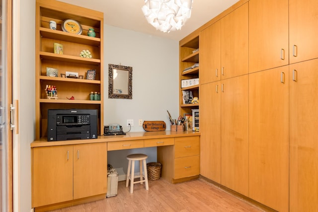 office space featuring an inviting chandelier, built in desk, built in shelves, and light hardwood / wood-style flooring