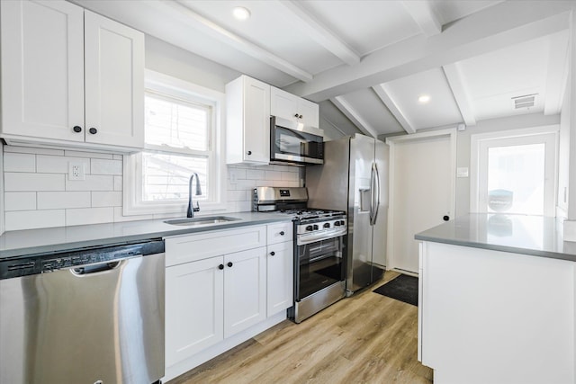 kitchen with appliances with stainless steel finishes, white cabinetry, sink, vaulted ceiling with beams, and light hardwood / wood-style flooring