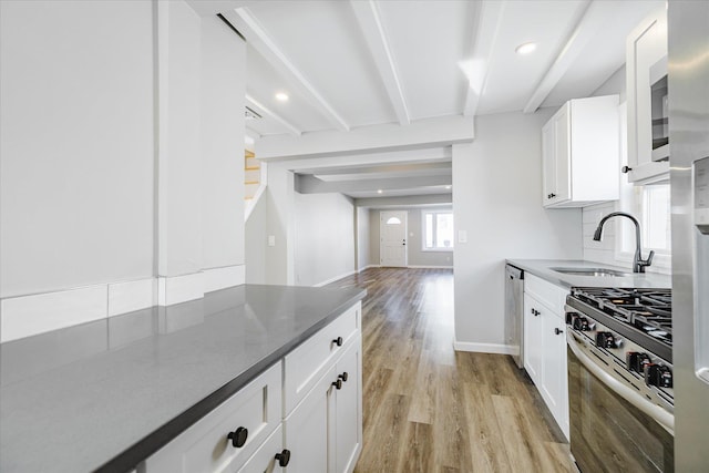 kitchen featuring stainless steel range with gas cooktop, beamed ceiling, sink, white cabinets, and light wood-type flooring