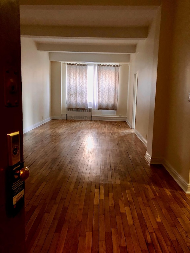 empty room with beamed ceiling, radiator, and hardwood / wood-style floors