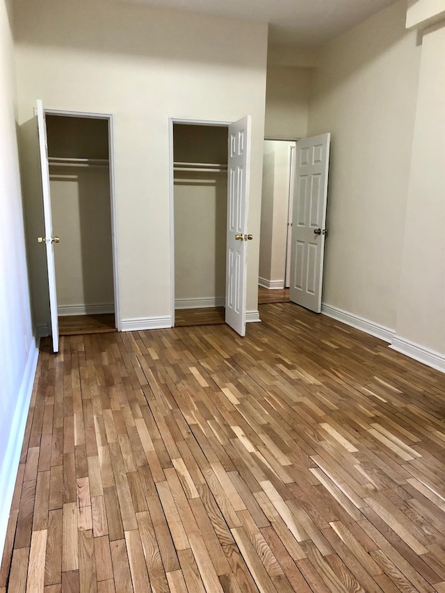 unfurnished bedroom with wood-type flooring and multiple closets