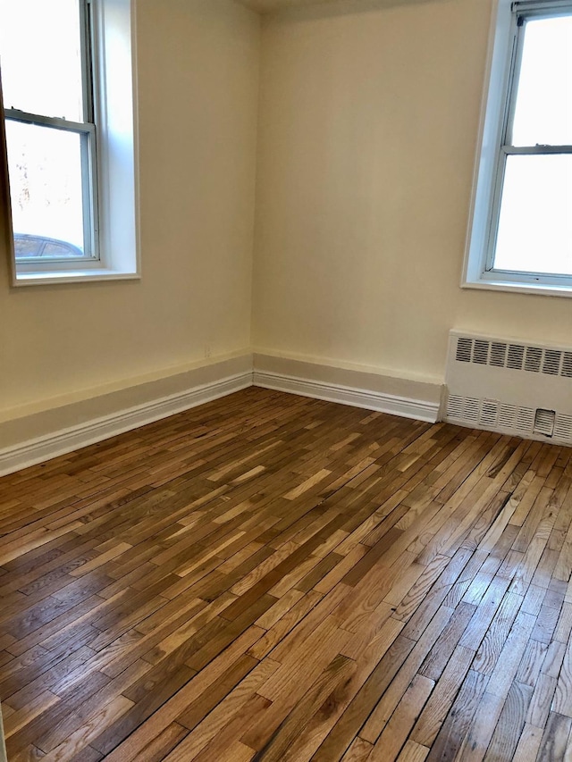 empty room with dark hardwood / wood-style flooring and radiator heating unit