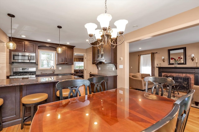 dining space with sink, a fireplace, a chandelier, and light wood-type flooring