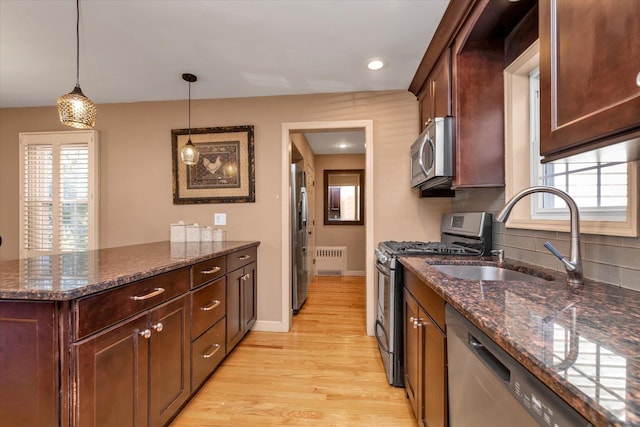 kitchen with appliances with stainless steel finishes, radiator, dark stone countertops, and decorative light fixtures