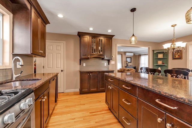 kitchen featuring sink, decorative light fixtures, light hardwood / wood-style flooring, dark brown cabinets, and dark stone countertops