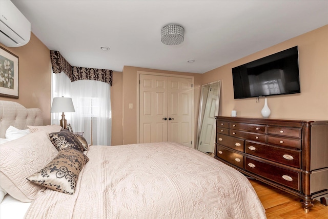 bedroom with a wall mounted air conditioner, a closet, and light wood-type flooring