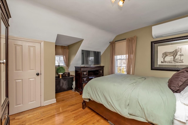 bedroom featuring lofted ceiling, a wall mounted air conditioner, and light hardwood / wood-style flooring