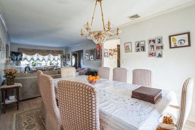 dining room with ornamental molding, visible vents, an inviting chandelier, and wood finished floors