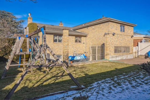 rear view of property with a playground, brick siding, fence, a yard, and a chimney