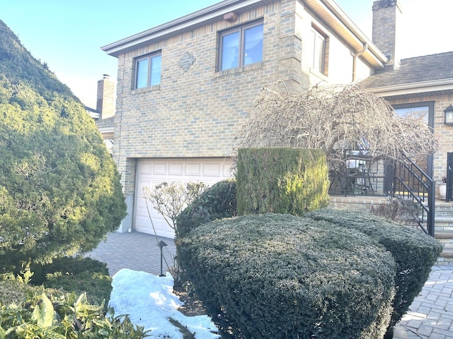 view of front facade featuring a garage, brick siding, and a chimney