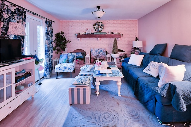 living room featuring a brick fireplace, french doors, brick wall, and light wood-type flooring